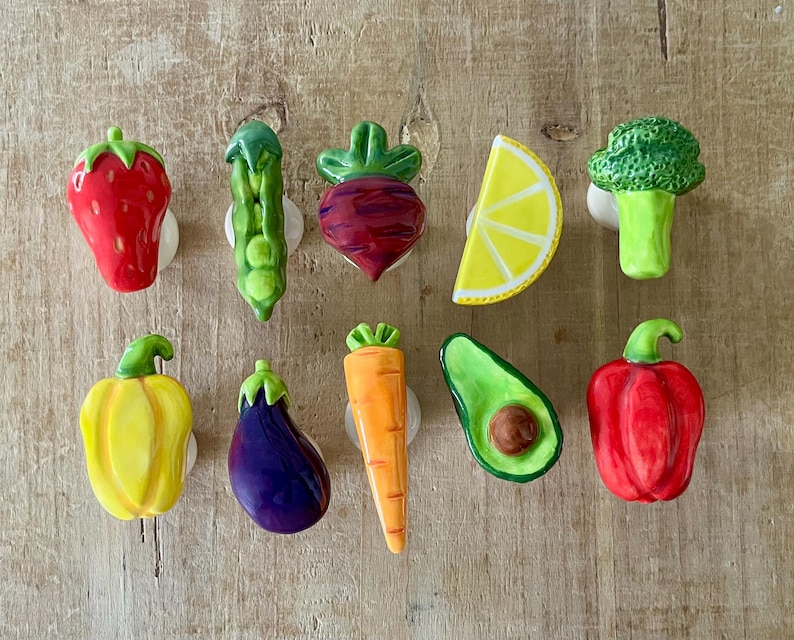 Pu&ograve; includere: Una collezione di pomelli per mobili in ceramica a forma di verdura colorata. Il set include una fragola rossa, un baccello di piselli verde, una barbabietola rossa, una fetta di limone giallo, broccoli verdi, peperone giallo, melanzana viola, carota arancione, avocado verde e peperone rosso.