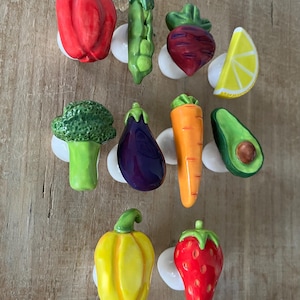 Pu&ograve; includere: Una collezione di pomelli per mobili in ceramica a forma di verdura e frutta. Il set comprende un peperone rosso, un baccello di piselli verdi, una barbabietola, una fetta di limone, broccoli, melanzane, carote, avocado, peperone giallo e fragola.