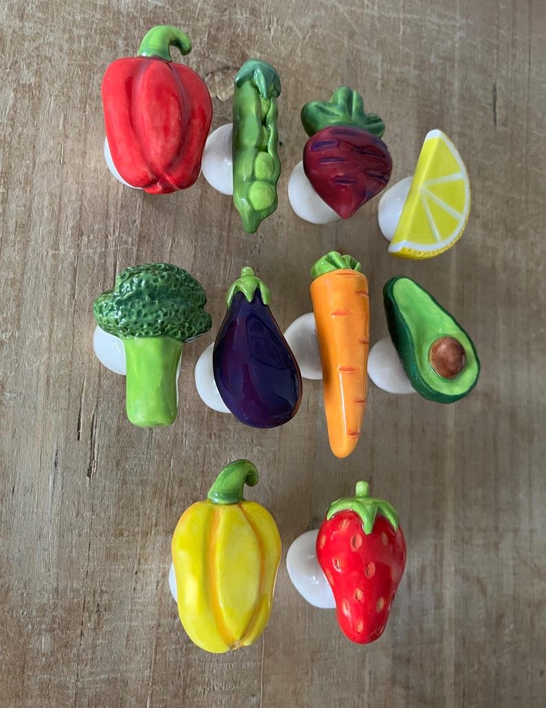 Pu&ograve; includere: Una collezione di pomelli per mobili in ceramica a forma di verdura e frutta. Il set comprende un peperone rosso, un baccello di piselli verdi, una barbabietola, una fetta di limone, broccoli, melanzane, carote, avocado, peperone giallo e fragola.