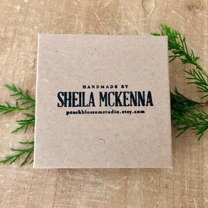 Puede incluir: Una caja cuadrada de color marr&oacute;n claro con el texto "HANDMADE BY SHEILA MCKENNA peachblossomstudio.etsy.com" impreso en negro. La caja est&aacute; sobre una superficie de madera, con ramitas verdes en el fondo.