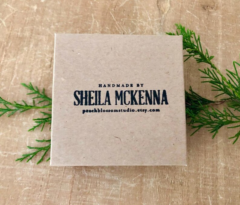 Puede incluir: Una caja cuadrada de color marr&oacute;n claro con el texto "HANDMADE BY SHEILA MCKENNA peachblossomstudio.etsy.com" impreso en negro. La caja est&aacute; sobre una superficie de madera, con ramitas verdes en el fondo.