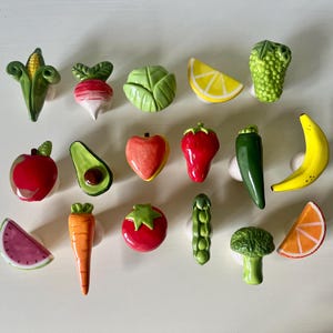 Pu&ograve; includere: Una collezione di diciassette pomelli per cassetti in ceramica a forma di vari frutti e verdure, tra cui mais, ravanello, cavolo, limone, uva, mela, avocado, pesca, fragola, peperoncino, banana, anguria, carota, pomodoro, piselli, broccoli e arancia.