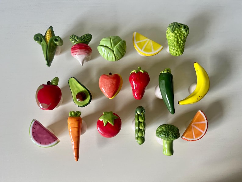 Pu&ograve; includere: Una collezione di diciassette pomelli per cassetti in ceramica a forma di vari frutti e verdure, tra cui mais, ravanello, cavolo, limone, uva, mela, avocado, pesca, fragola, peperoncino, banana, anguria, carota, pomodoro, piselli, broccoli e arancia.