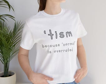 May include: White t-shirt with the word "'tism" and the phrase "because 'normal' is overrated" printed in black. The shirt has short sleeves and a crew neck.