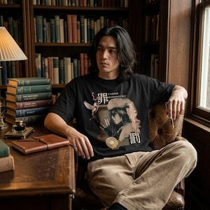 Può includere: T-shirt nero con grafica di Fëdor Dostoevskij, testo giapponese e illustrazione di una gru. La persona è seduta su una poltrona di pelle in una biblioteca, con libri e una lampada da scrivania.