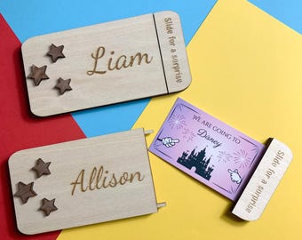 May include: Wooden slide-out surprise boxes with names "Liam" and "Allison" engraved on them, each with star accents. One box reveals a card that says "We are going to Disney". The text "Slide for a surprise" is also visible.
