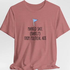 May include: A heather red t-shirt with a small blue flag graphic and the text "MARKED SAFE (BARELY) FROM POLITICAL ADS".
