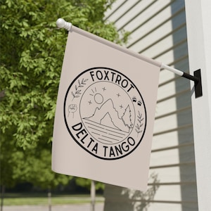 May include: A beige flag with a black and white logo. The logo is a circle with the words "Fox Trot Delta Tango" around the outside. Inside the circle is a mountain range, a sun, a tree, a fist, and paw prints.