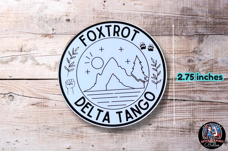 Puede incluir: Una pegatina redonda blanca y negra con el texto "FOXTROT DELTA TANGO" en un c&iacute;rculo. La pegatina presenta una monta&ntilde;a, un sol, dos &aacute;rboles y un pu&ntilde;o. La pegatina tiene un di&aacute;metro de 2,75 pulgadas.