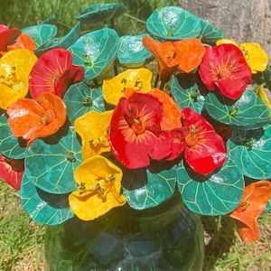 Pode incluir: Um vibrante buquê de flores de papel feitas à mão em um vaso de vidro verde. As flores são em tons de vermelho, laranja e amarelo, com folhas verdes. O arranjo é colocado em um fundo natural ao ar livre.