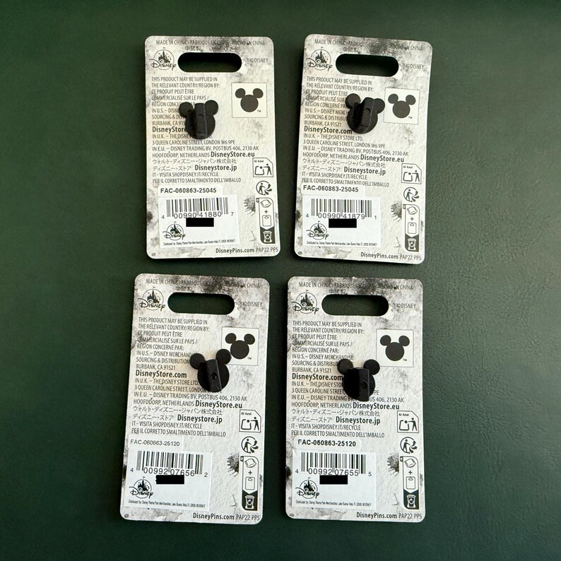 May include: Four Disney pins on their original backing cards. Each card is white with black text and a black Mickey Mouse head silhouette. The pins are black and shaped like Mickey Mouse's head. The cards have a hole at the top for display.