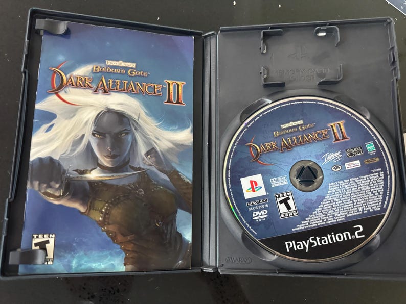 May include: A PlayStation 2 game case for Baldur's Gate: Dark Alliance II. The front cover features a female elf character holding a dagger. The back cover shows the game's logo and a description of the game.