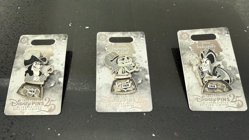May include: Three Disney character pins on grey backing cards. Each pin shows a character with an inkwell, and the word "INK". The cards read "Disney Pins 25 Limited Edition". A collectible set for Disney fans.