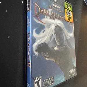 May include: A PlayStation 2 video game case for Dark Alliance II, a role-playing game set in the Forgotten Realms universe. The case features a female character with white hair and a sword, and the title "Dark Alliance II: Baldur's Gate" is prominently displayed. The game is rated Teen by the ESRB.