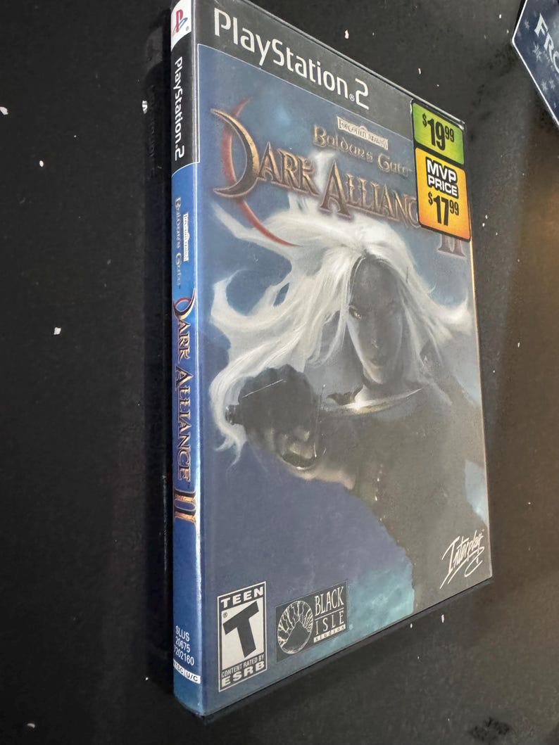 May include: A PlayStation 2 video game case for Dark Alliance II, a role-playing game set in the Forgotten Realms universe. The case features a female character with white hair and a sword, and the title "Dark Alliance II: Baldur's Gate" is prominently displayed. The game is rated Teen by the ESRB.