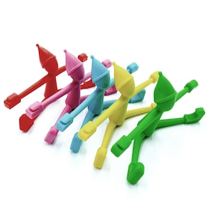 May include: A selection of colourful silicone wine charms in red, pink, blue, yellow, and green. Each charm is shaped like a small figure with outstretched arms and a pointed hat, designed to identify wine glasses.