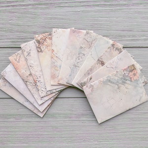 May include: A set of ten delicate, pale pink envelopes with a subtle floral pattern. The envelopes are arranged in a fan shape on a light wood surface.
