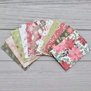 May include: A collection of rectangular greeting cards arranged in a fan shape, featuring various holiday-themed patterns including red poinsettias, white snowflakes, green pine needles, candy canes, and plaid designs in shades of red, green, and white.