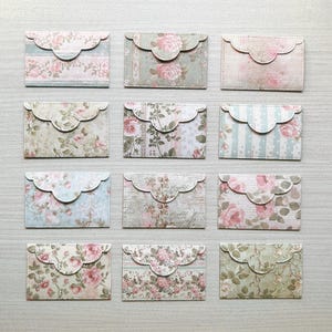 May include: A collection of twelve rectangular paper envelopes arranged in a grid, each featuring a scalloped flap and a unique floral pattern in various soft pastel shades including pink, green, blue, and cream with botanical rose motifs.