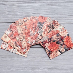 May include: A fan of rectangular paper envelopes featuring a repeating floral pattern in shades of deep red, orange, and muted cream. The envelopes are arranged in a semi-circular display, showcasing the dense botanical print of roses and leaves.