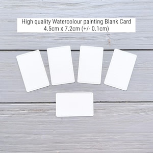 May include: Five white rectangular blank cards for watercolor painting, each measuring 4.5cm x 7.2cm (+/- 0.1cm). The cards feature rounded corners and a smooth surface, arranged in a fan-like pattern with one card positioned horizontally below.