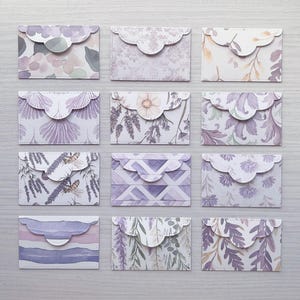 May include: Twelve small rectangular paper envelopes with scalloped flaps, arranged in a grid. Each envelope features a unique pattern in shades of purple, lavender, and white, including floral, botanical, geometric, and bee-themed designs.