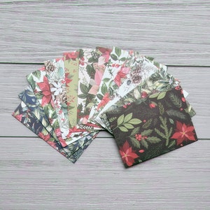 May include: A collection of rectangular paper envelopes arranged in a fan shape. Each envelope features a distinct holiday-themed pattern, including illustrations of red poinsettias, green pine needles, holly berries, and pinecones on various backgrounds.