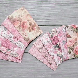 Op de afbeelding: Twee sets bloemenpatroon papieren vellen uitgewaaierd op een grijze houten ondergrond. De vellen hebben een verscheidenheid aan roze en crèmekleurige bloemenontwerpen, waaronder rozen. Het papier heeft een vintage, romantische uitstraling.