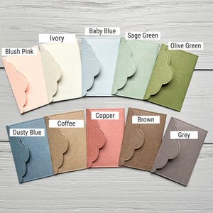 May include: A collection of ten rectangular felt card holders with scalloped envelope-style flaps, labeled in colors: Blush Pink, Ivory, Baby Blue, Sage Green, Olive Green, Dusty Blue, Coffee, Copper, Brown, and Grey, arranged in two rows.