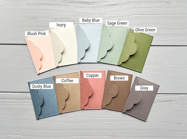May include: A collection of ten rectangular felt card holders with scalloped envelope-style flaps, labeled in colors: Blush Pink, Ivory, Baby Blue, Sage Green, Olive Green, Dusty Blue, Coffee, Copper, Brown, and Grey, arranged in two rows.