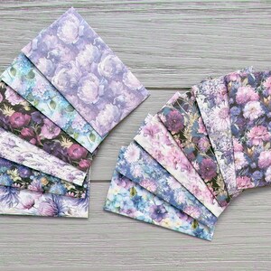 Op de afbeelding: Een verzameling rechthoekige enveloppen gerangschikt in twee waaiervormige groepen. Elke envelop heeft een bloemenpatroon in tinten paars, blauw, roze en wit, met diverse bloemsoorten zoals pioenrozen en hortensia's.