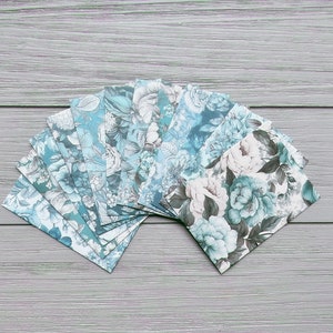 May include: A collection of rectangular paper envelopes arranged in a fan shape, each featuring a detailed floral pattern in shades of teal, blue, white, and dark grey. The envelopes display various botanical illustrations of blooming flowers and leaves.