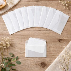 May include: Several white rectangular envelopes are displayed on a wooden surface. One envelope is open, showing a white, textured card. The envelopes are arranged neatly, possibly for stationery or packaging.