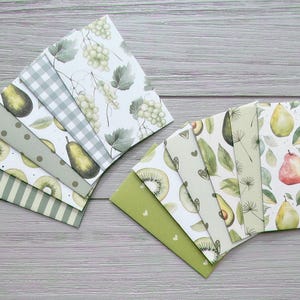May include: A collection of rectangular paper envelopes arranged in two fan-shaped clusters. The envelopes feature various patterns including watercolour illustrations of green grapes, pears, kiwi slices, avocados, and leaves, alongside stripes, dots, and gingham.