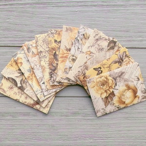 May include: A set of 10 decorative envelopes featuring a floral design in shades of yellow, brown, and white. The envelopes are arranged in a fan shape on a light wood surface.