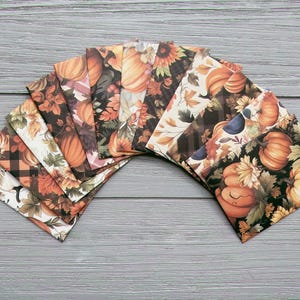 May include: A fan-shaped arrangement of square paper envelopes featuring various autumn-themed patterns. The designs include illustrations of orange pumpkins, sunflowers, and fall foliage in shades of brown, cream, black, and green, with some featuring plaid patterns.