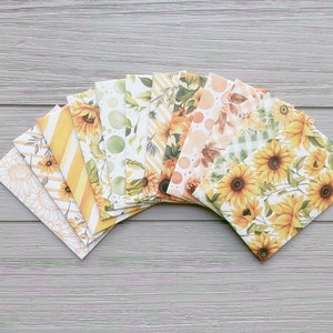 May include: A collection of ten rectangular envelopes arranged in a fan shape, featuring various patterns including yellow sunflowers, green foliage, diagonal stripes, polka dots, and gingham checks in shades of yellow, green, white, and brown.