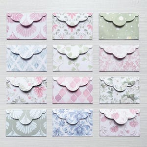 May include: A collection of twelve small rectangular paper envelopes arranged in a grid. Each envelope features a unique pattern, including floral, geometric, and botanical designs in soft pastel shades of pink, green, blue, and white.
