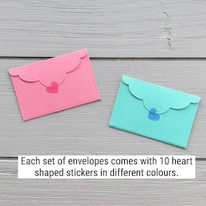May include: Two rectangular envelopes with scalloped flaps, one in pink and one in teal, each featuring a small heart-shaped sticker. The text states: Each set of envelopes comes with 10 heart shaped stickers in different colours.