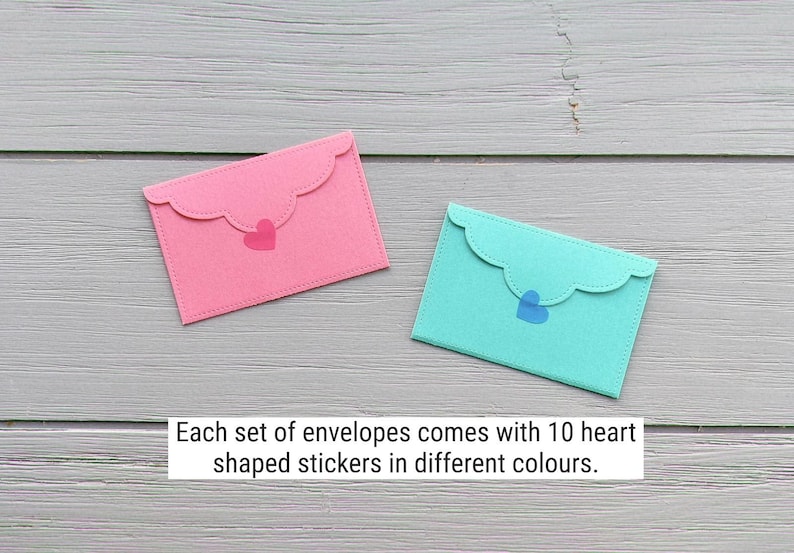 May include: Two rectangular envelopes with scalloped flaps, one in pink and one in teal, each featuring a small heart-shaped sticker. The text states: Each set of envelopes comes with 10 heart shaped stickers in different colours.