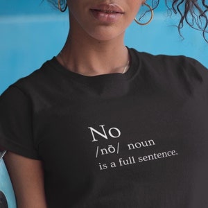May include: Black t-shirt with the word "No" and its phonetic pronunciation, followed by "noun is a full sentence" in white text. The person is wearing gold hoop earrings and a striped skirt. The background is a light blue.