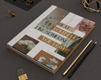 May include: A white notebook with a brown border and floral collage on the cover. The text on the cover reads "Treat Yourself Like Someone You Love" and "2026 Daily Notebook".