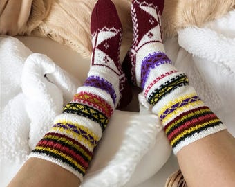 May include: A pair of white and burgundy knitted socks with colorful stripes and geometric patterns. The socks are worn on a person's feet.