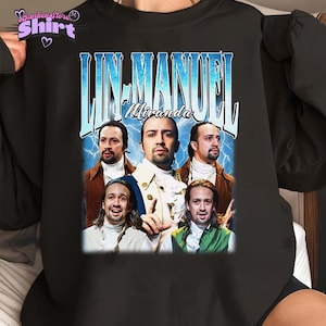 May include: Black crew neck sweatshirt featuring a graphic of Lin-Manuel Miranda with the text "Lin-Manuel Miranda" in a vintage style. The design includes multiple images of the actor and a blue lightning bolt background.