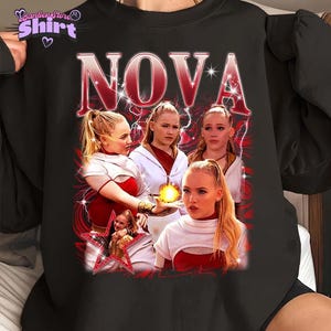 May include: Black sweatshirt with a retro design featuring the word "NOVA" in red. The graphic includes images of women with blonde hair, wearing red and white outfits, and a star. The shirt has the text "Panther Star Shirt" in the upper left corner.