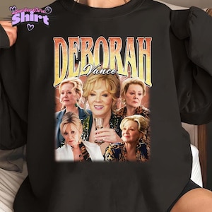 Op de afbeelding: Zwarte sweatshirt met een afbeelding van Deborah Vance met de tekst "Deborah Vance" in vintage stijl. De afbeelding bevat meerdere afbeeldingen van de actrice. De sweatshirt heeft een ronde hals en lange mouwen.