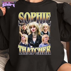 May include: Black sweatshirt with a graphic print of a group of people. The text "Sophie Thatcher" is printed in yellow letters.