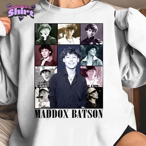Puede incluir: Sudadera blanca de cuello redondo con un collage de imágenes de una persona. El nombre "MADDOX BATSON" está impreso en negro en la parte inferior. La camiseta también tiene un logotipo de "Panther Star Shirt" en la parte superior izquierda. Las imágenes son en blanco y negro.