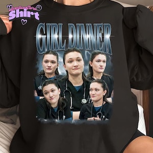 Könnte beinhalten: Schwarzes Sweatshirt mit einer Grafik einer Frau in mehreren Posen, die ein Stethoskop trägt. Der Text "GIRL DINNER" wird in einer stilisierten Schriftart über dem Bild angezeigt. Das Sweatshirt hat einen Rundhalsausschnitt.