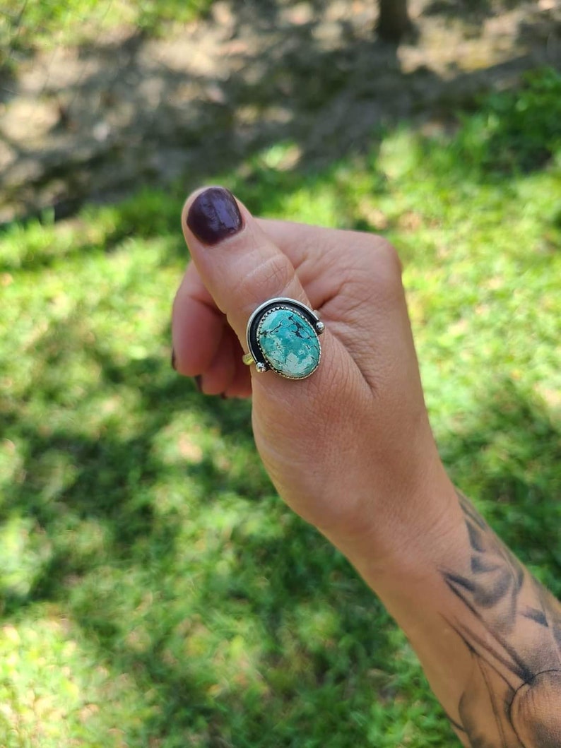 May include: A silver ring with a turquoise stone set in a curved band.